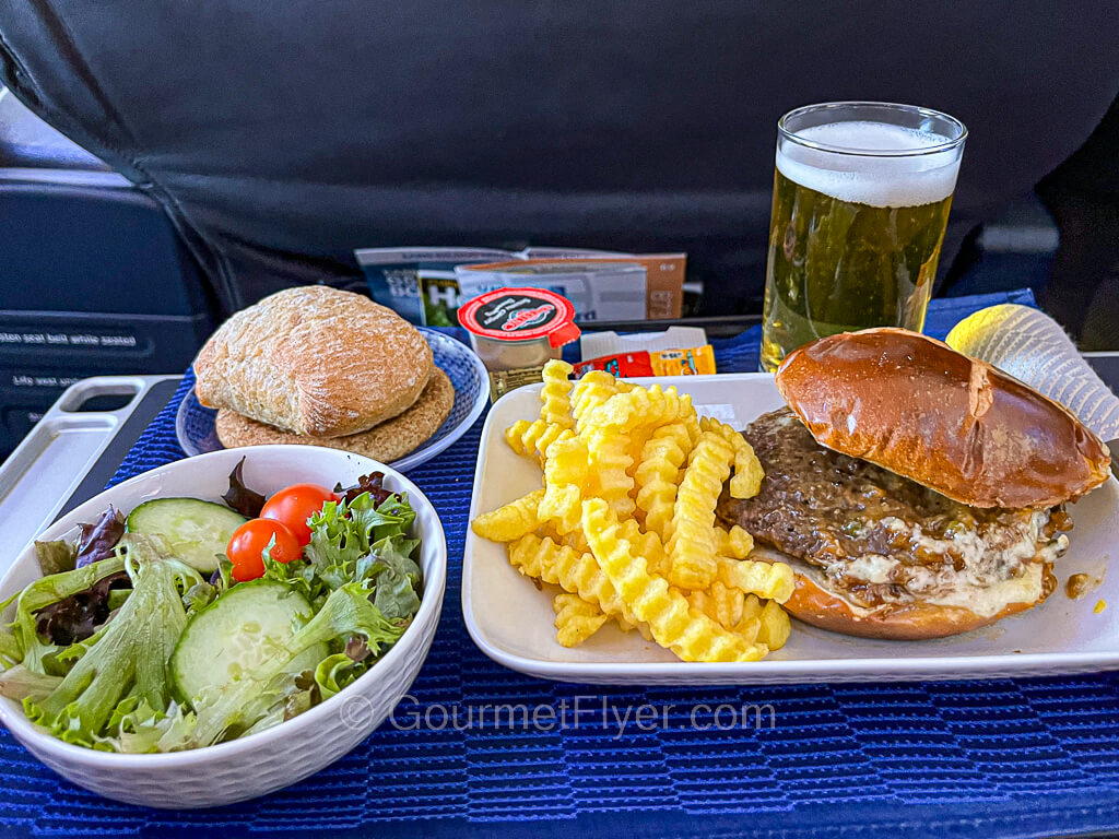 A dinner tray with burger and fries is served with a green salad and accompanied by a tall glass of beer.