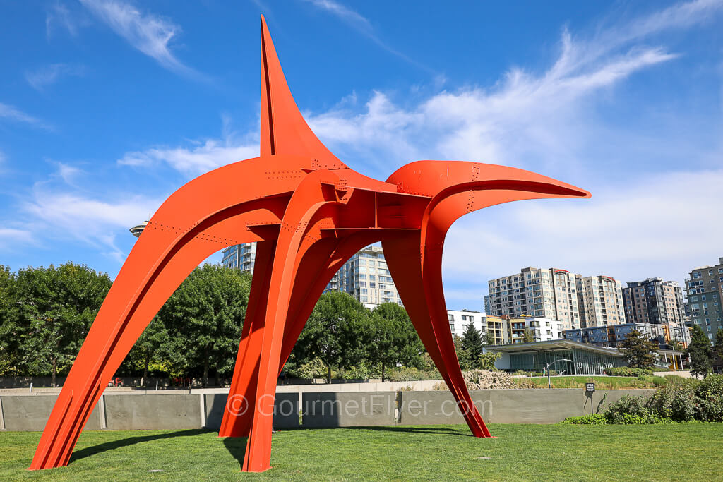 A red sculpture with an artsy expression of an eagle sits on a grass area.