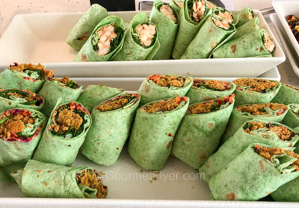 A long tray of falafel wraps is accompanied by another tray of chicken wraps.