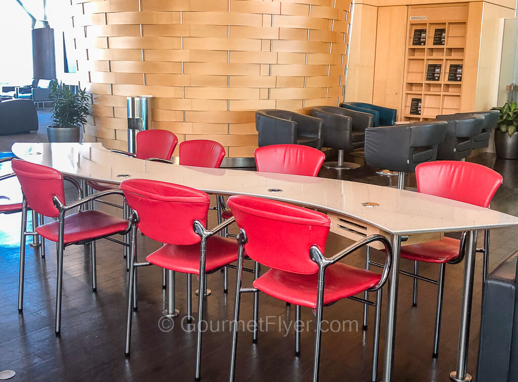 A long stylish and curvy table is accompanied by 7 red diner type chairs. 