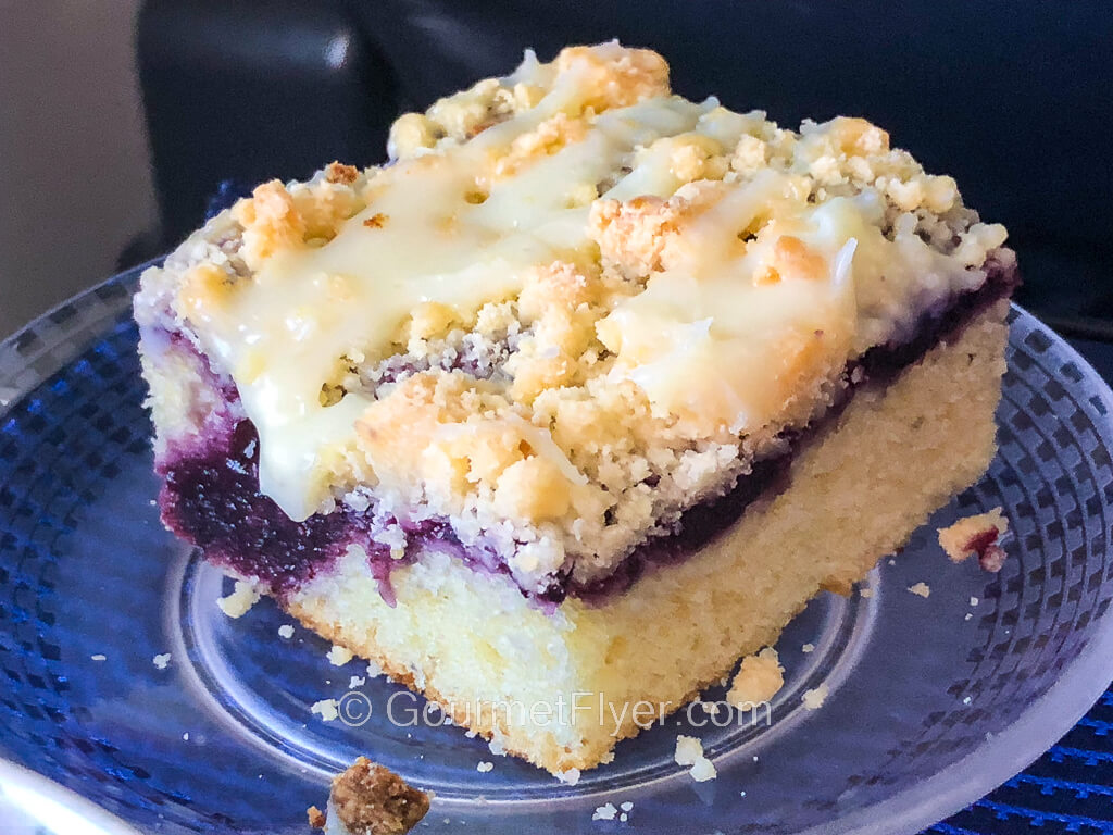 A square slice of shortcake has blueberry fillings and is topped with a yellowish lemon frosting.