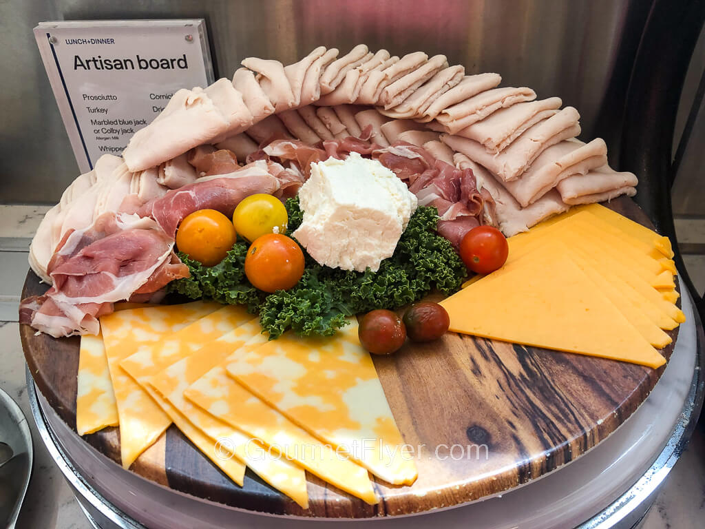 A board of sliced prosciutto, turkey, and cheeses are garnished with several cherry tomatoes.