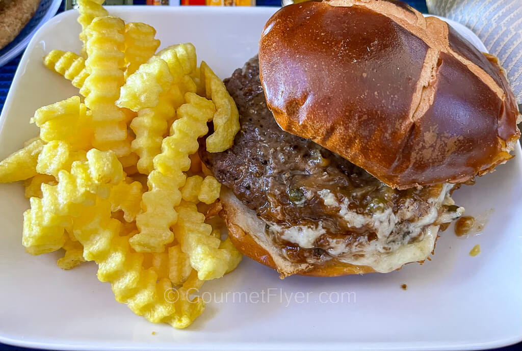 A burger has its crown slid open is served on a plate accompanied by crinkle cut fries.