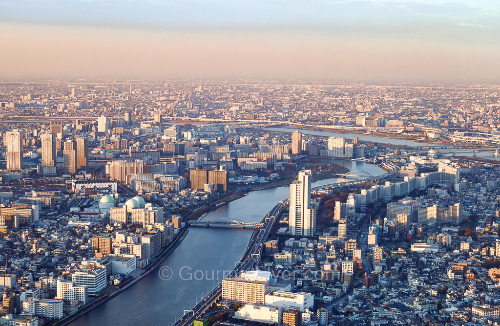 The city of Tokyo separated by the river running through it is viewed from the Skytree during dusk.