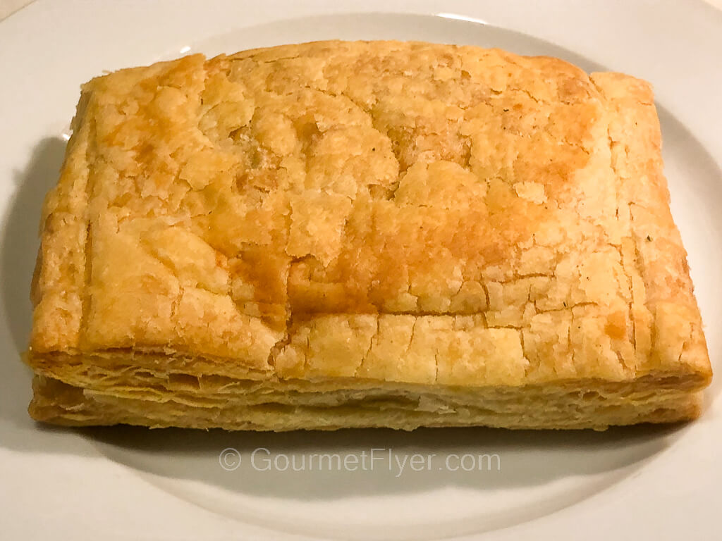 A rectangular shaped baked pastry with a golden-brown crust is served on a plate.