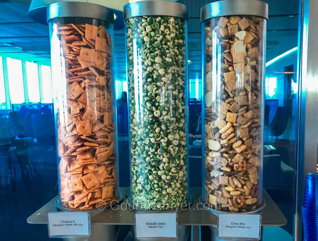 Three tall glass canisters are filled with, from left to right, Cheeze-It, wasabi peas, and Chex Mix.