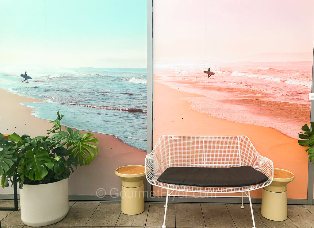 Two large blown-up colorful photos of the shadow of a surfer carrying a surfboard walking into the sea are posted on the wall.