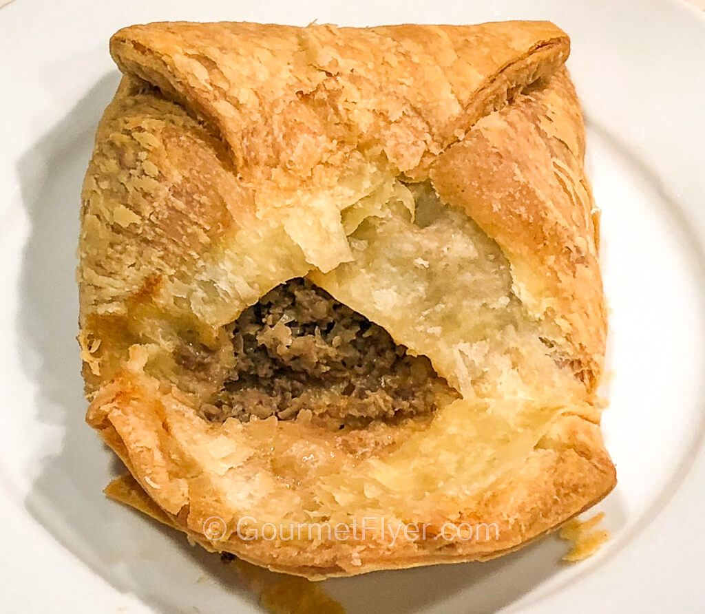 A hand pie with a golden-brown crust has one of its flaps flipped open to display its beef and onion filling.