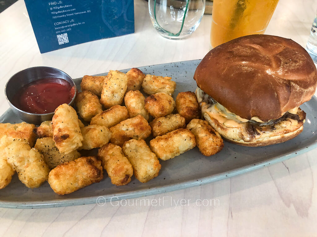 A burger is served on a long platter filled with tater tots.