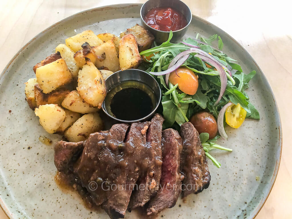 A sliced steak is served on a plate with potatoes and a green salad.