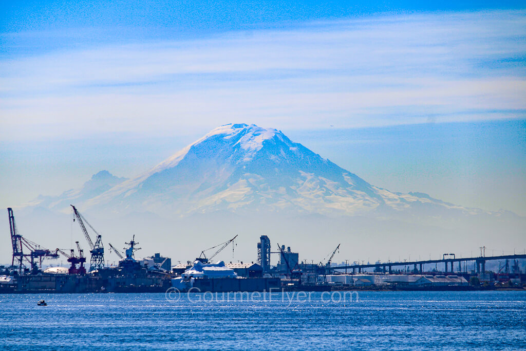 The volcano Mount Rainier can be seen in a hazy blue sky with the container ship terminal in the foreground.