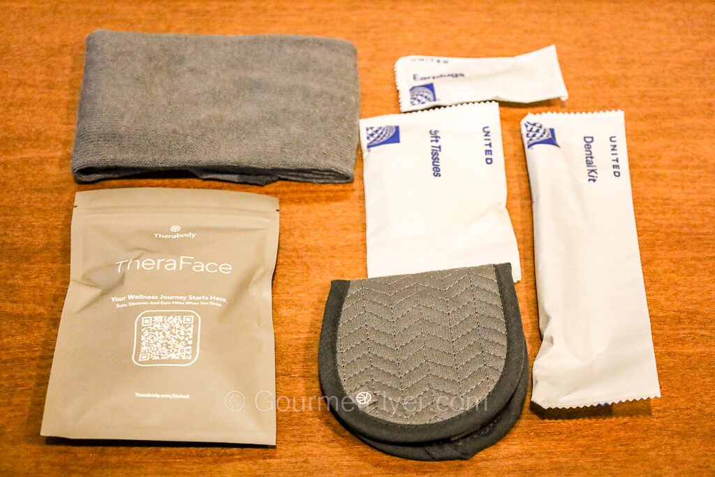 Socks, a skincare pouch, eye shade, and packages of other amenities are placed on a table.