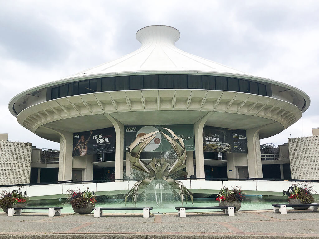 A spaceship-like structure has a metal sculpture located in front of it, built on a water fountain.