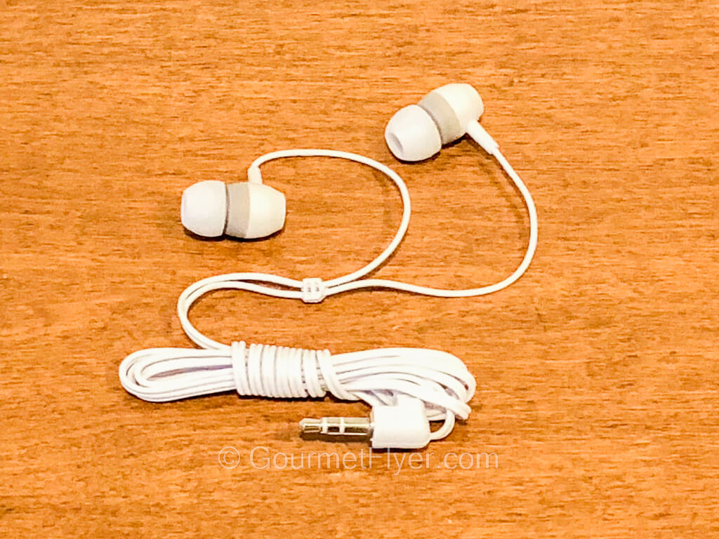 A pair of earbuds with white wirings sit atop a wooden desk.