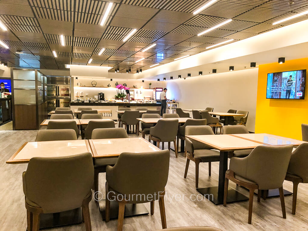 A seating area with about a dozen rectangular wooden dining tables with chairs are located near the buffet stations.