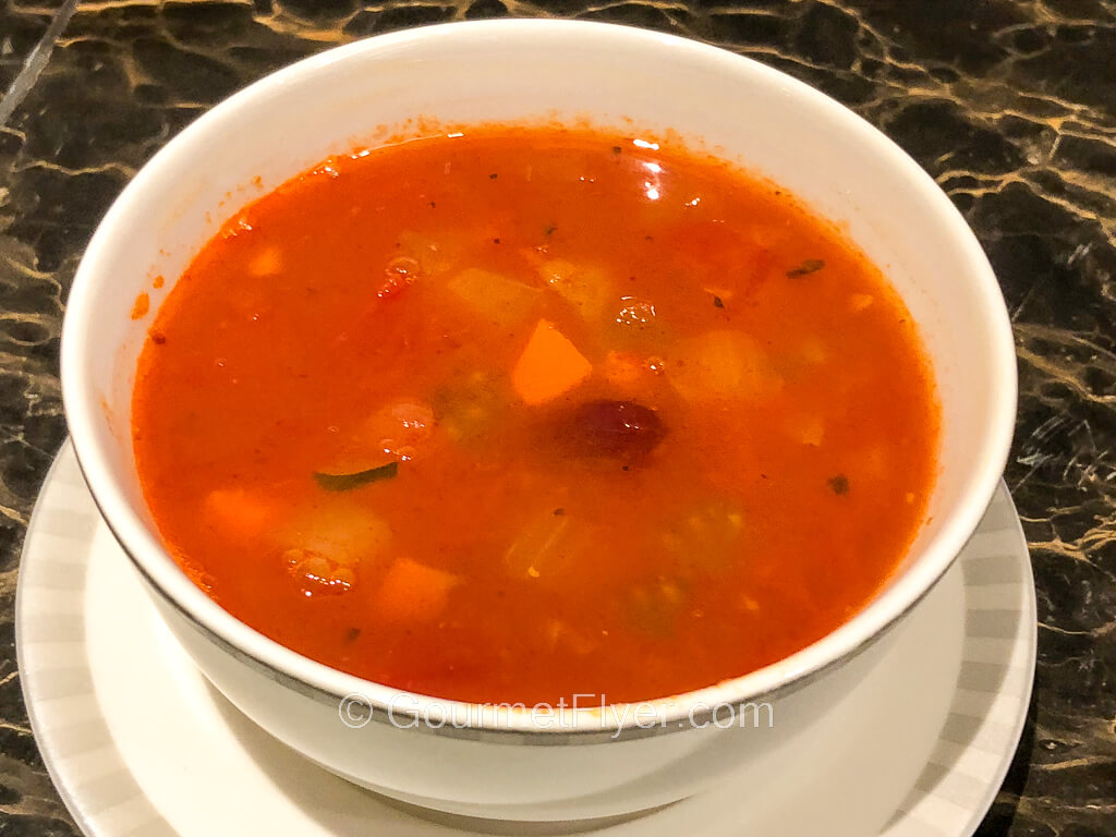 A bowl of red tomato-based soup has plenty of chopped vegetables in it.