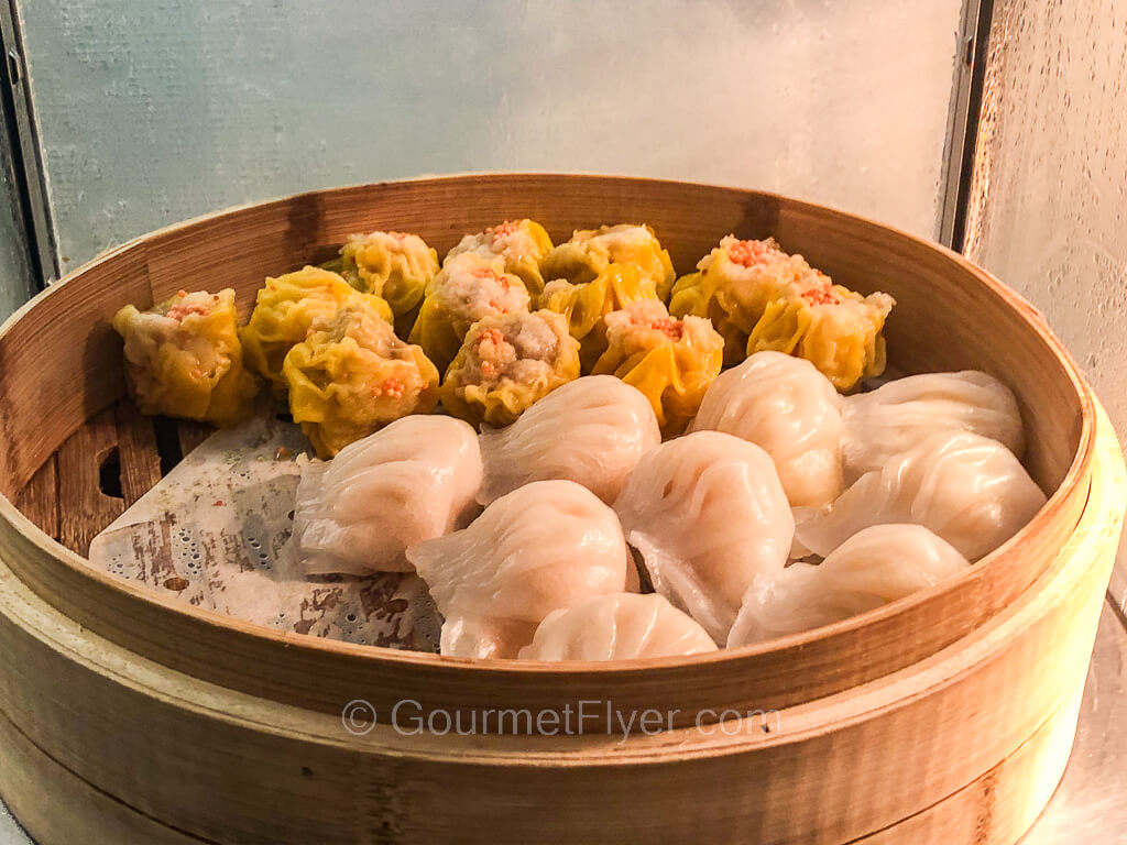 A bamboo steamer is filled with shrimp dumplings in front and pork dumplings in the back.