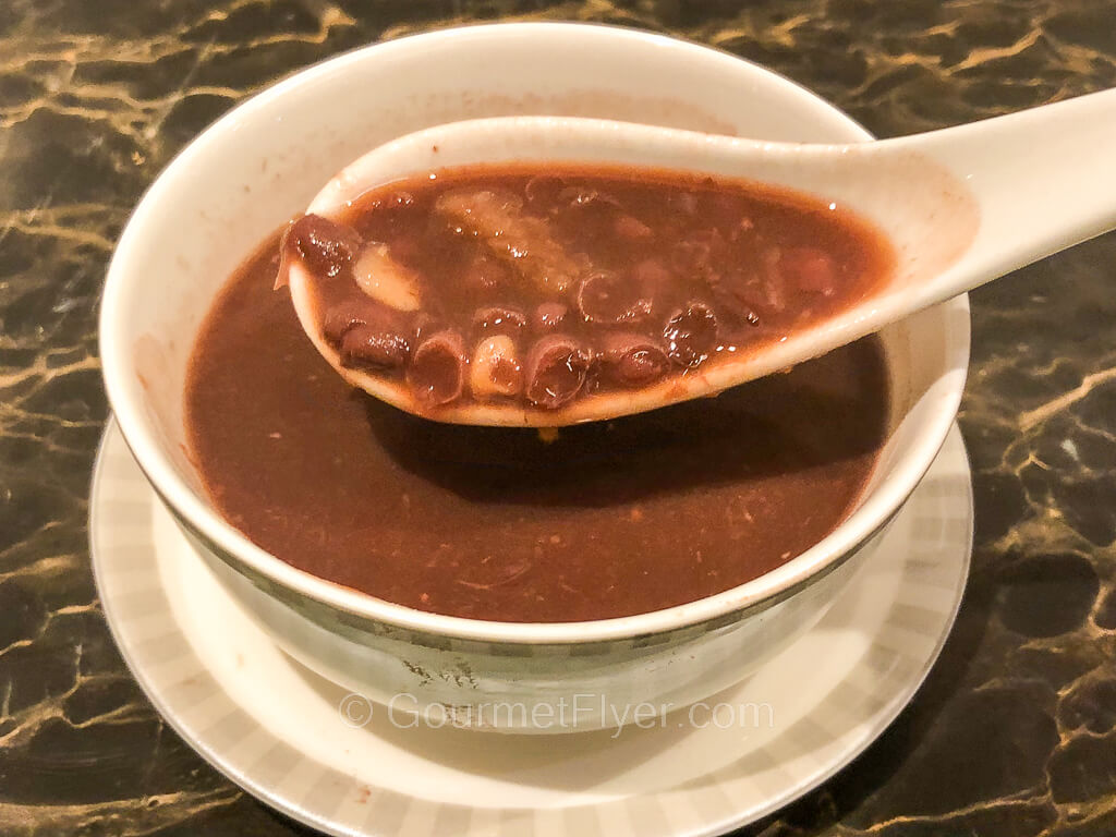 A spoon on top of a bowl of red bean soup displays the ingredients of the soup.