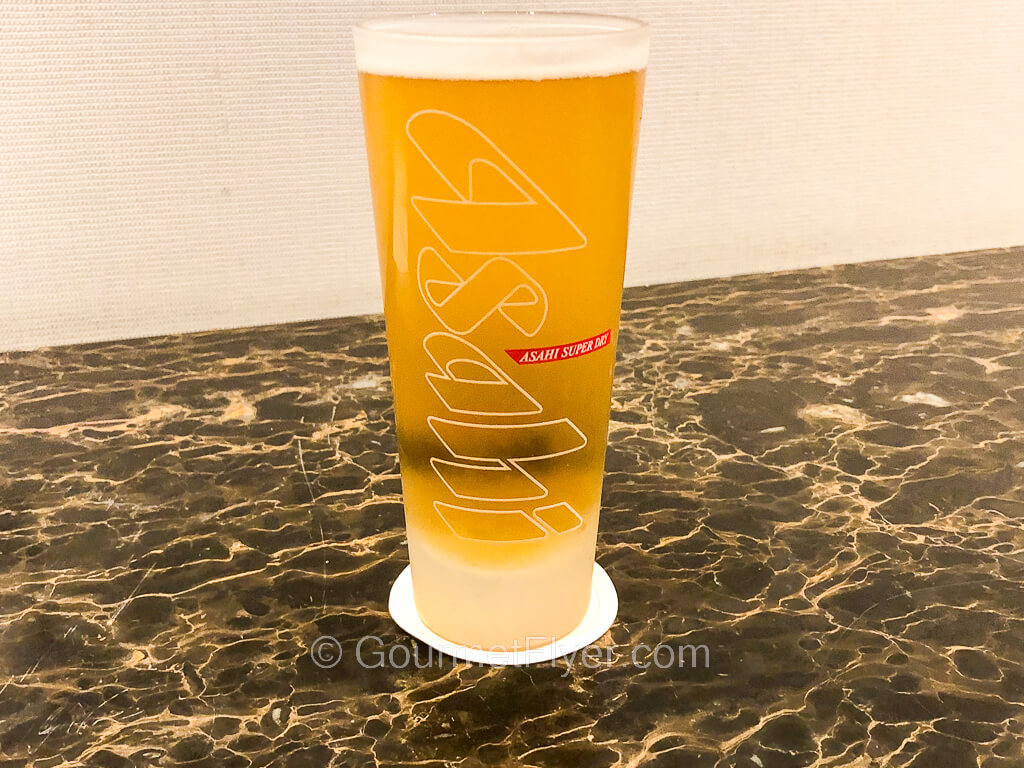 A tall flute-like glass of beer with the Asahi logo sits on top of a marble counter.