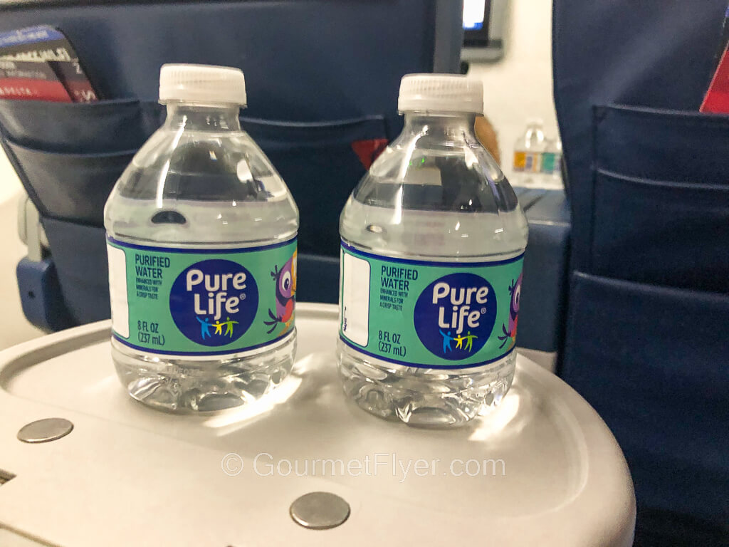 Two small bottles of water sit atop an extended beverage area on the armrests of first class seats.