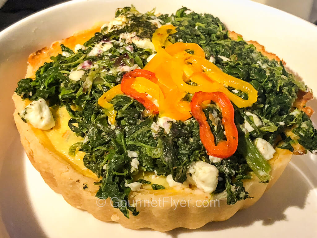 A round pie-like quiche with spinach and various colors of peppers on top.