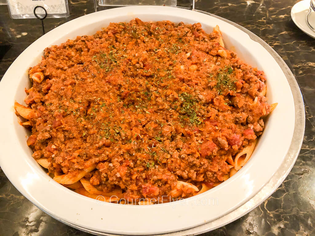 A chafing dish contains pasta covered in a red meat sauce garnished with sprinkles of parsley. 