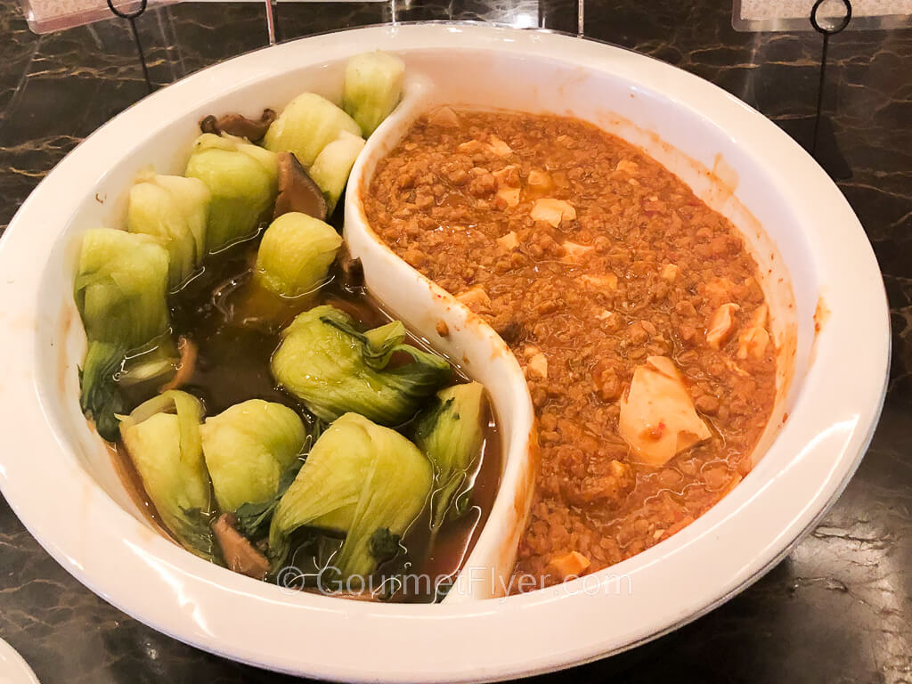 A partitioned serving bowl contains Chinese vegetables on the left and tofu in a red sauce on the right.