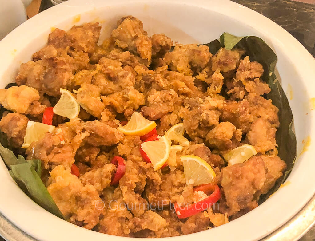 A large bowl of fried battered meats is garnished with lemon wedges and bits of red peppers.