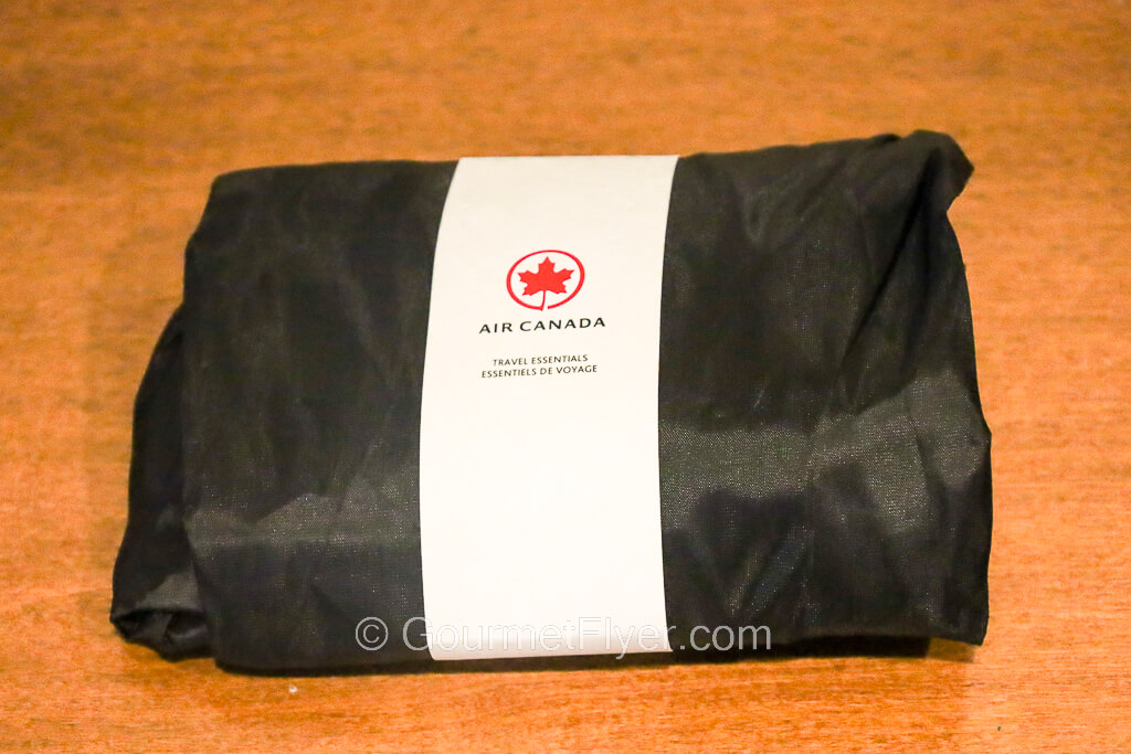 An amenity kit is rolled up and bound by a paper folder with Air Canada's red maple leaf logo on it.