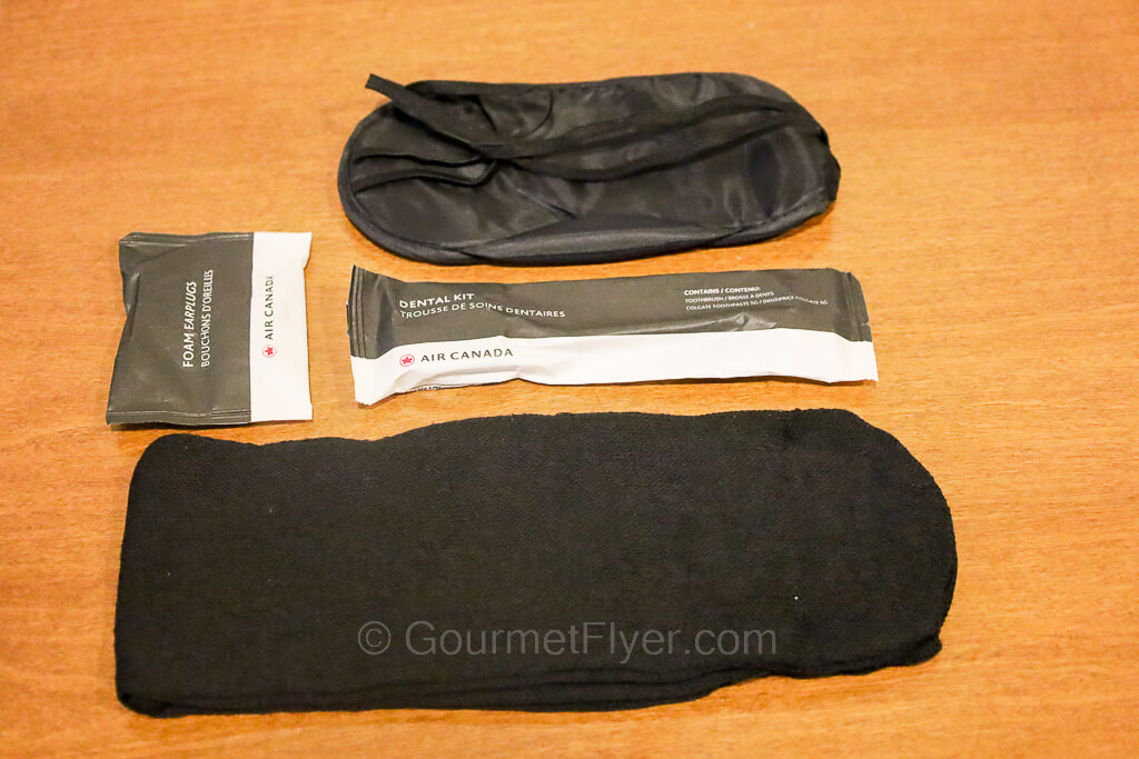 The contents of the amenity kit from top to bottom are eyeshades, earplugs, dental kit, and a pair of socks.