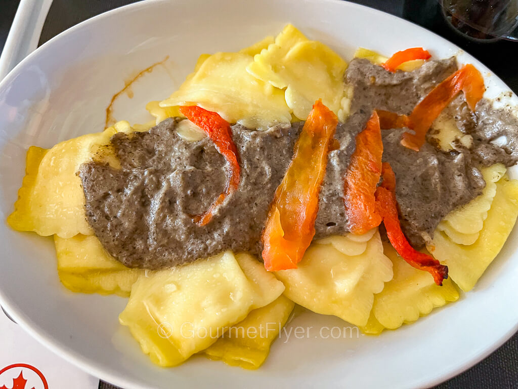 A plate of ravioli is topped with brown mushroom gravy and shredded red peppers.