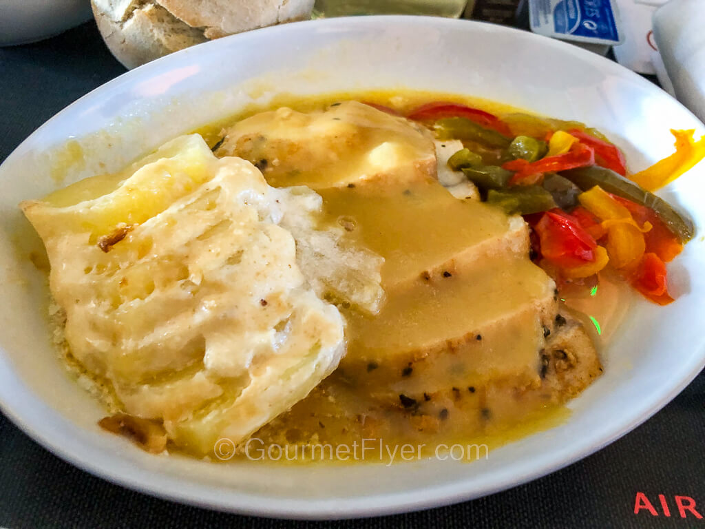 A plate of sliced chicken breast meat topped with gravy is accompanied by sliced potatoes and mixed vegetables.