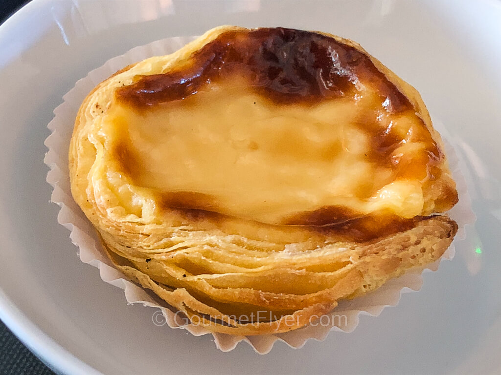An egg custard tart dessert with the top slightly burnt is served on a plate.