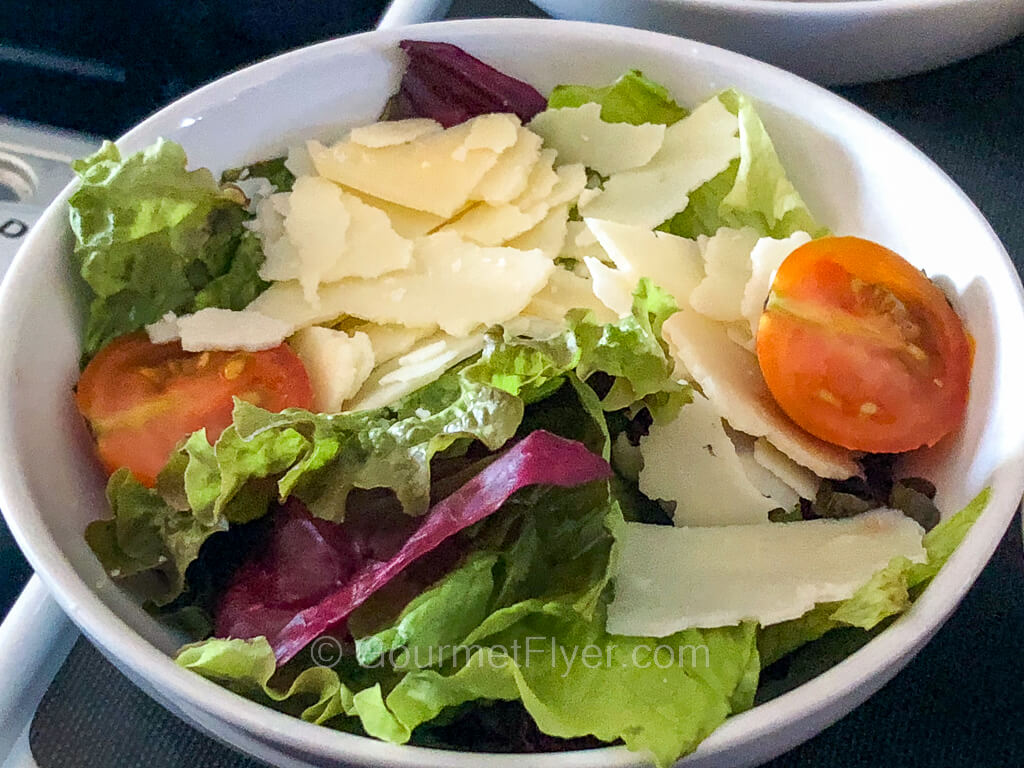 A bowl of green lettuce is topped with cherry tomatoes and fresh cheese.