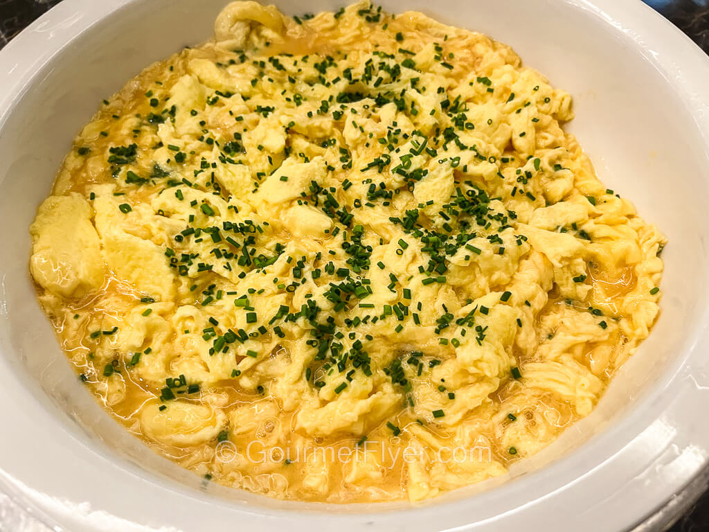 A serving platter is filled with scrambled eggs that are garnished with chives.
