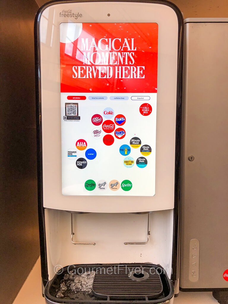 A soda machine displays over a dozen icons of various soft drinks on its screen.