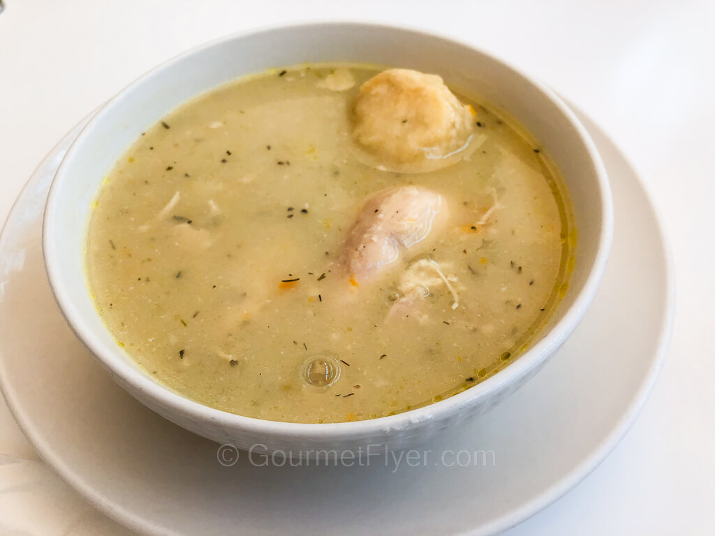A greenish colored creamy soup is served in a small cup.