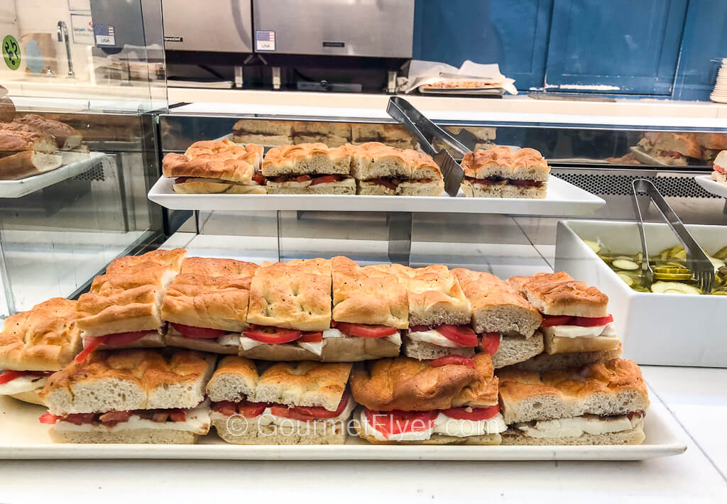 A long tray is stacked with two layers of tomato slices and cheese sandwiched between focaccia bread.