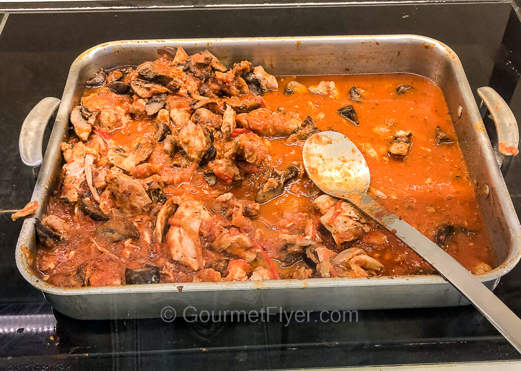 A tray of shredded chicken meat braised in a red tomato-based sauce is served in an aluminum pan.
