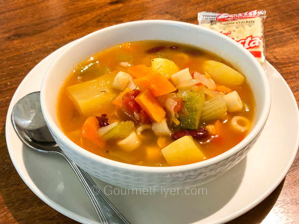 A tomato-based soup served in a bowl is loaded with lots of cut vegetables.