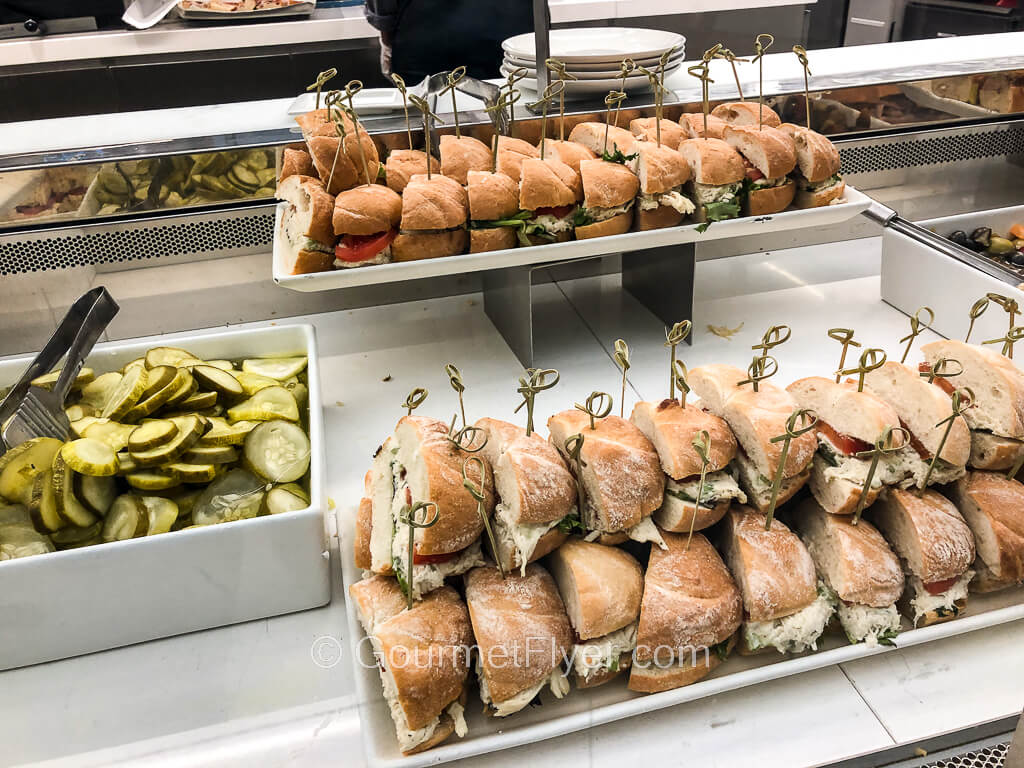 A long tray is stacked with layers of chicken salad sandwiches in rolls that are cut in half.
