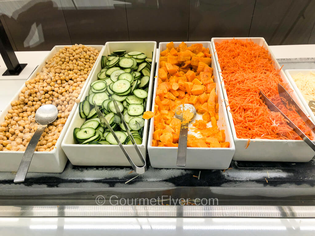 Four long narrow trays of vegetables are placed side by side to form part of a salad bar.