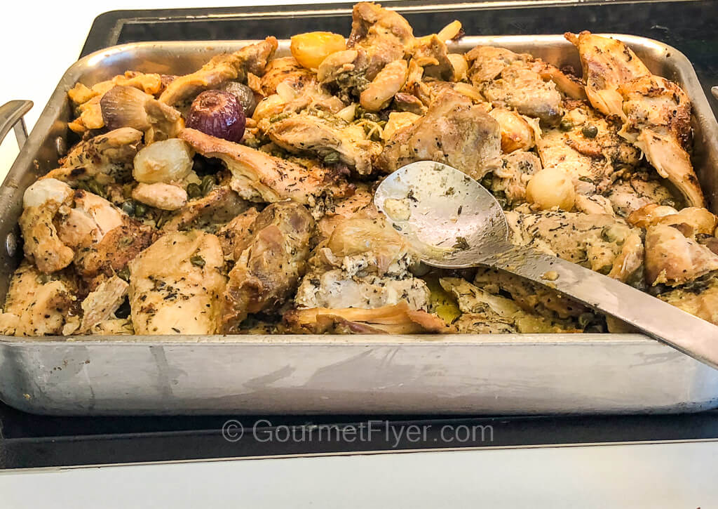 A large aluminum tray is filled to the top with cuts of chicken meat tossed in  sauce with spices.
