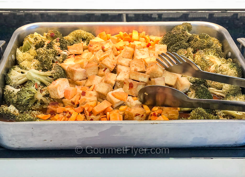A large serving of cubed tofu in the center of a dish is accompanied by broccoli on its sides.
