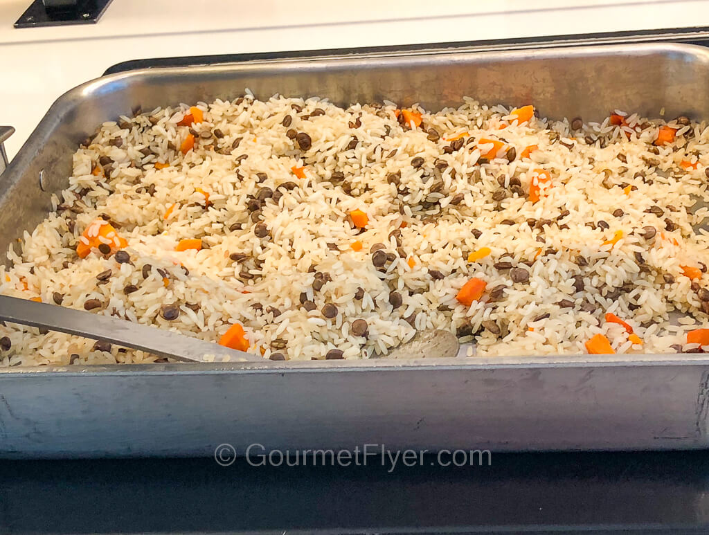 A serving dish is filled with a rice pilaf blended with some mixed vegetables.