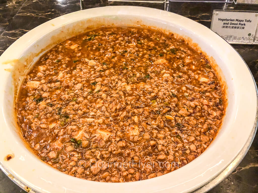 A large round serving bowl is filled to the brim with bits of tofu in a red sauce mixed with what appear to be minced pork.