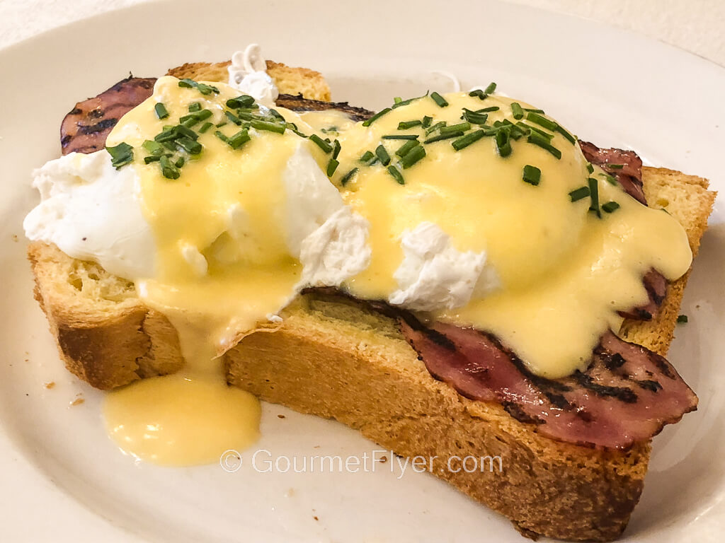 Two poached eggs topped with a yellowish sauce sit atop slices of bacon on a piece of bread.
