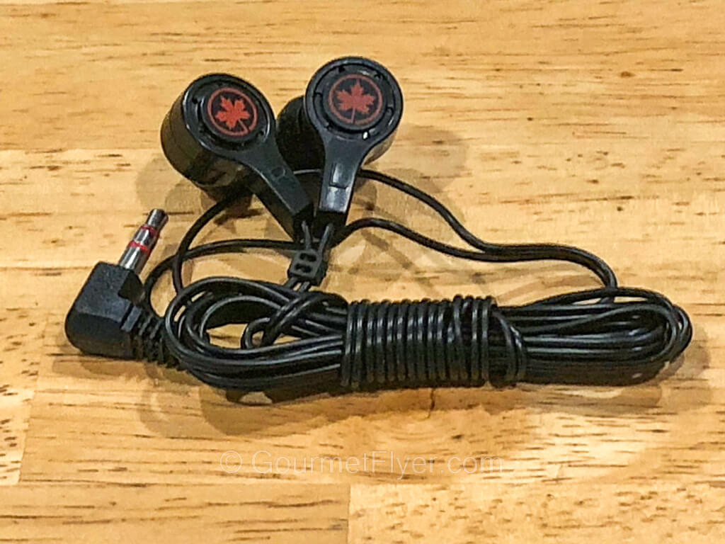 A pair of earbuds with a red maple leaf logo on each earpiece, and long neatly folded black wires that lead to a single prong 3.5mm jack.