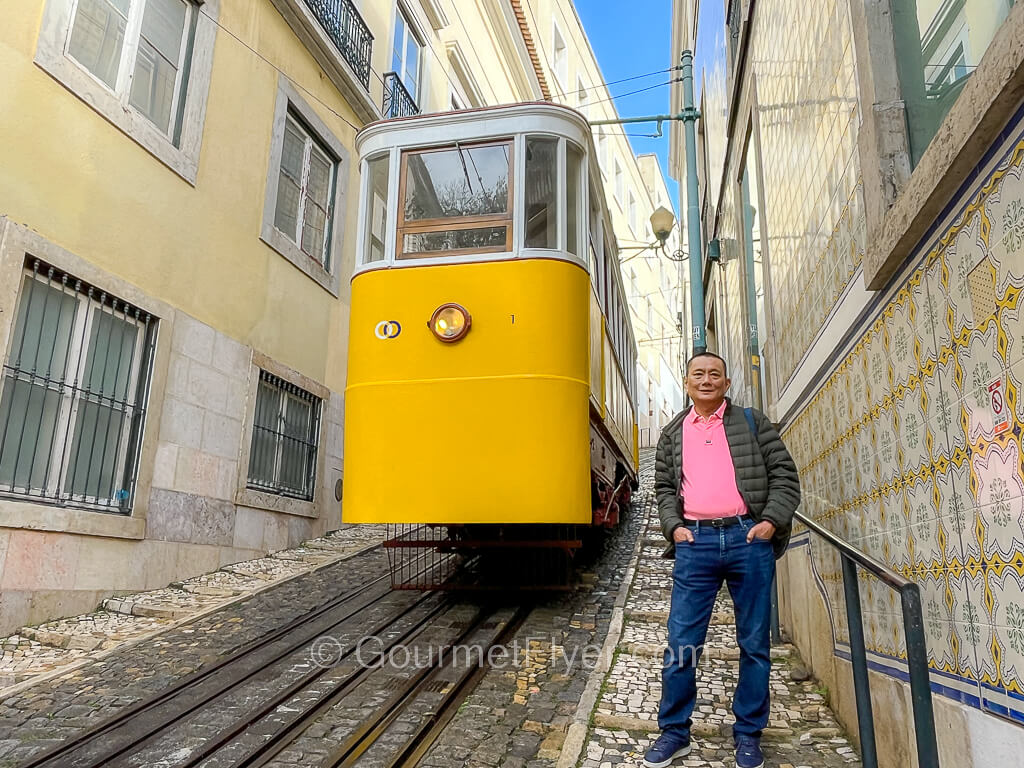A man, the Gourmet Flyer, is posing next to a yellow funicular car.