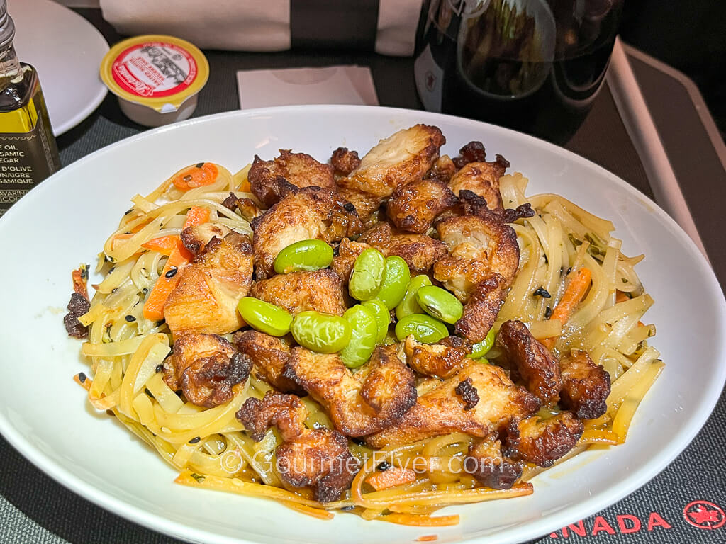 A plate of browned cubed chicken meat is served with creamy noodles and topped with edamame. 
